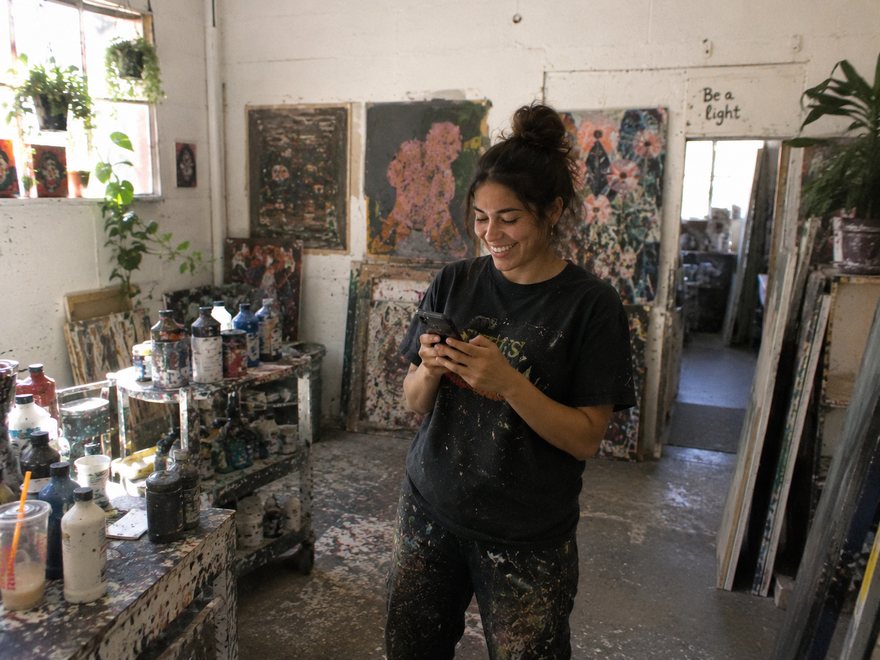 An artist working in their studio surrounded by paintings